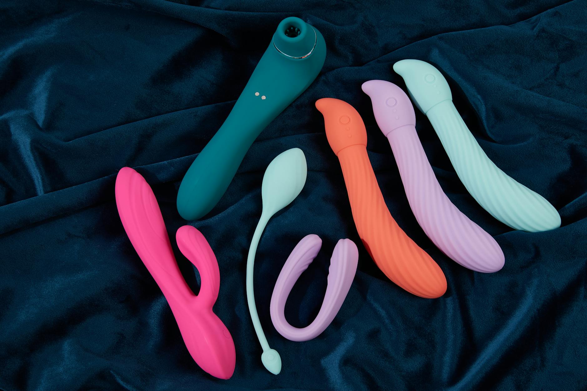 Collection of colorful silicone sex toys and clitoral vibrators on dark fabric background
