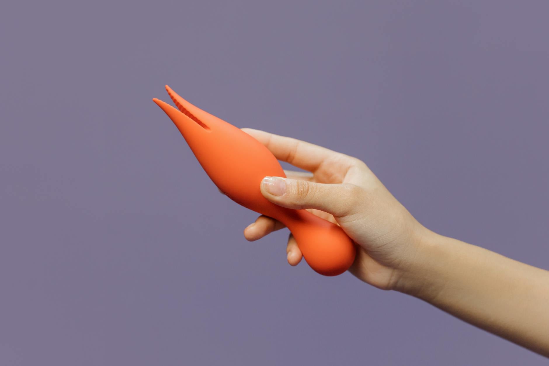 A hand holding a lemon-colored vibrator against a minimalistic purple backdrop, showcasing modern sensuality