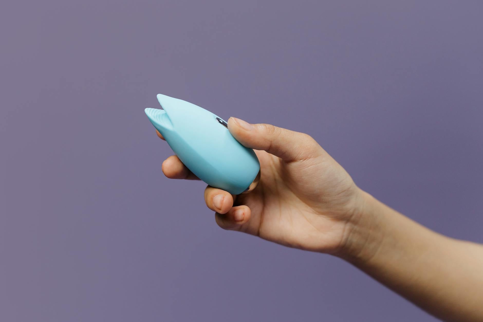 A hand holding a blue silicone sex toy on a purple background, symbolizing self-connection and embodied pleasure