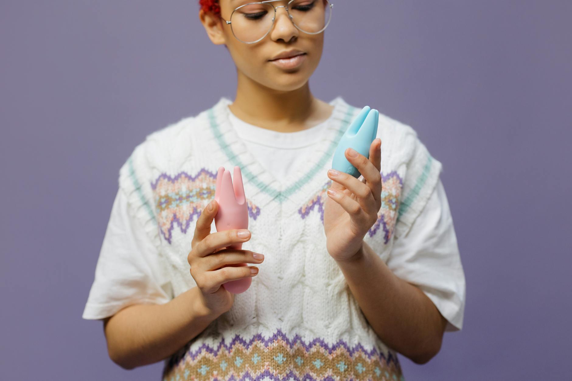 Close-up of hands holding a sleek blue silicone clitoral vibrator against a purple background